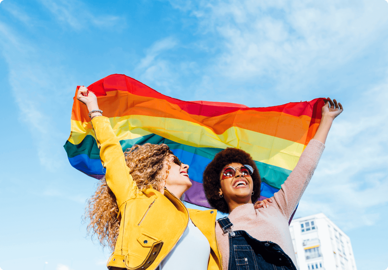 Imagem de duas pessoas sorrindo segurando a bandeira que representa a comunidade L G B T Q I A P N mais